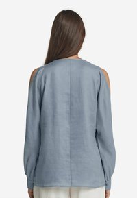 Blusa di lino azzurro chiaro con maniche lunghe, design con spalle scoperte, scollatura rotonda semplice e schiena dritta.