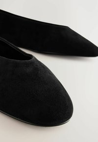 Musta mokkanahka ballet-kengät, joissa on terävä kärki, sileä rakenne ja minimalistinen tyyli ilman näkyviä varusteita tai koristeita.