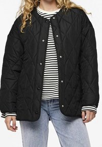 Black quilted jacket with snap buttons, featuring a round neckline. Worn over a black and white striped shirt, with light blue jeans.