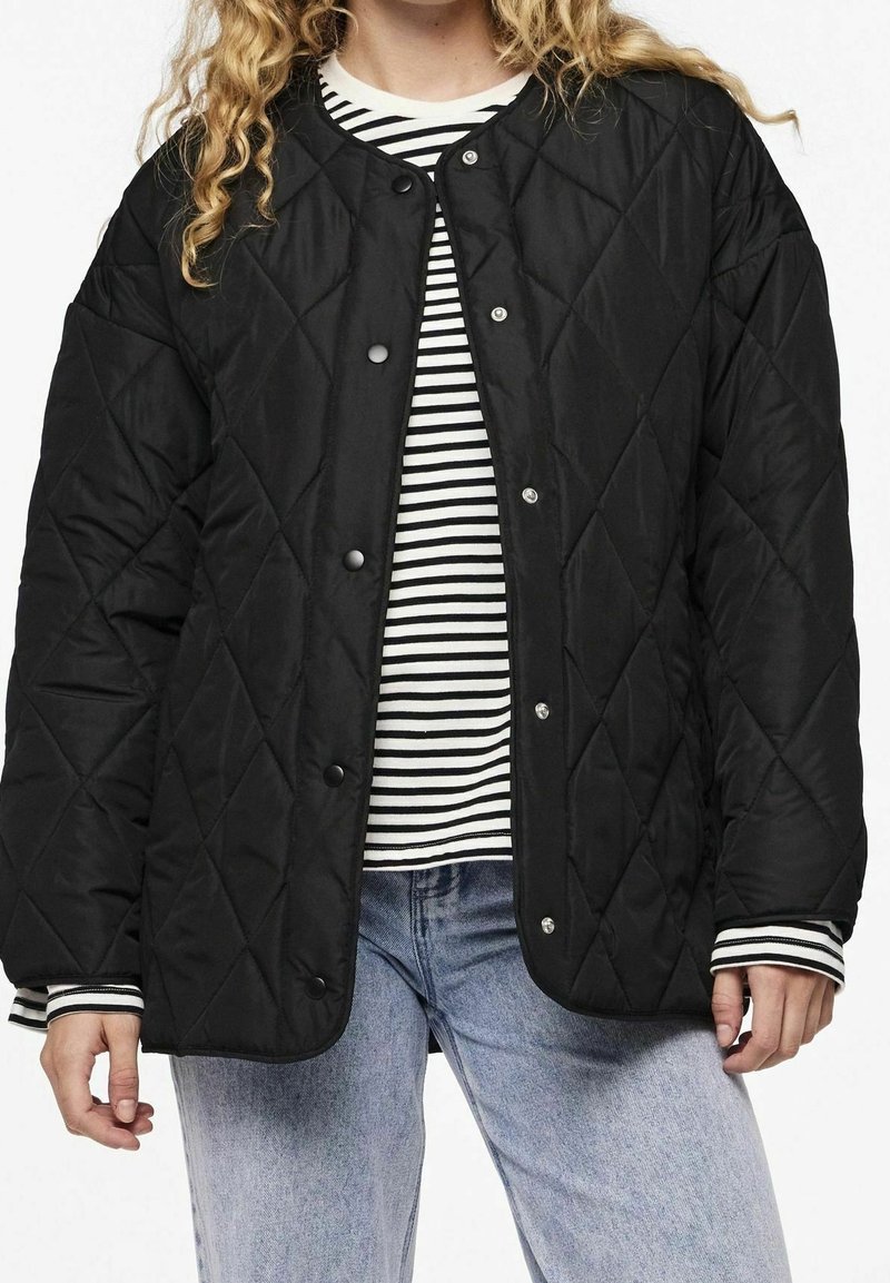 Black quilted jacket with snap buttons, featuring a round neckline. Worn over a black and white striped shirt, with light blue jeans.