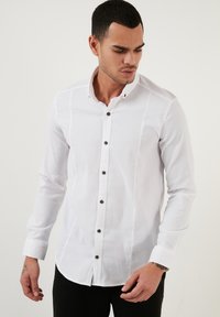 Hvid langærmet skjorte med struktureret stof, der har en knapnede krave og brune knapper langs stolpen. Slim fit design.