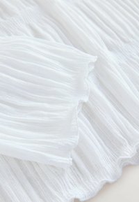 White pleated fabric with a soft, lightweight texture. The fabric has a delicate, sheer quality and features fine, horizontal folds.