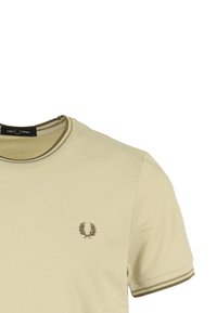 T-shirt beige a maniche corte con scollo rotondo, caratterizzato da strisce diagonali di colore verde oliva a contrasto e un piccolo emblema ricamato sul petto.