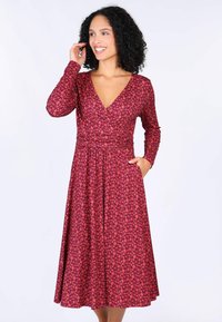 Rotes Blumenkleid mit langen Ärmeln, V-Ausschnitt und Taschen. Fließender Stoff mit einer taillierten Taille und einem Rock, der bis zur Mitte der Waden reicht.
