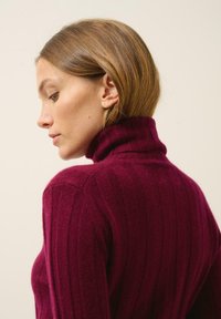 Suéter de cuello vuelto burdeos acanalado con una textura suave, que presenta un escote alto y una silueta ajustada, mostrado de lado.