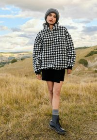 Jachetă cu model houndstooth alb-negru, asortată cu o fustă neagră și cizme negre cu șireturi. Modelul poartă o beretă gri și șosete gri.