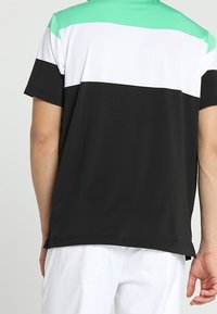 T-shirt à manches courtes avec un design en blocs de couleur vert, blanc et noir. Confectionné en tissu lisse et respirant.