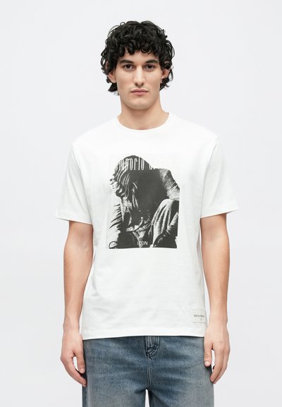 Λευκό βαμβακερό t-shirt με μαύρο γραφικό τύπωμα καθιστής φιγούρας. Κοντά μανίκια, στρογγυλή λαιμόκοψη και μικρή ετικέτα στο τελείωμα.