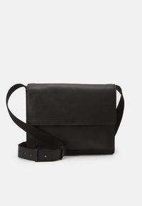 Borsa a tracolla in pelle nera con ampia cinturino regolabile e chiusura a pattina su sfondo bianco semplice.