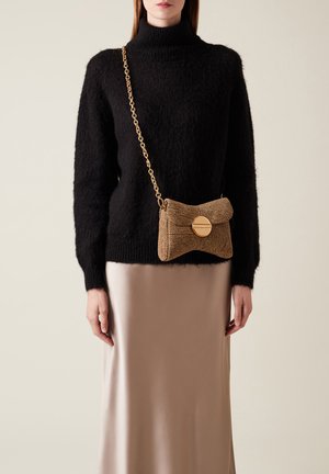 Brown textured handbag with a chain strap and a circular gold clasp, worn over a black sweater and beige satin skirt.