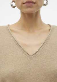Beiger V-Ausschnittpullover mit feiner Stricktextur und gerippten Kanten. Der Halsausschnitt ist weich und das Material wirkt leicht.