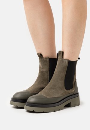 Botines de ante verde con paneles elásticos laterales negros, punta redondeada y suela gruesa de goma. La parte superior presenta detalles a juego en cuero.