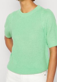 Jasnozielony sweter z krótkimi rękawami i okrągłym dekoltem. Posiada teksturowane wykończenie oraz luźny krój. Duża elastyczność i oddychający materiał.
