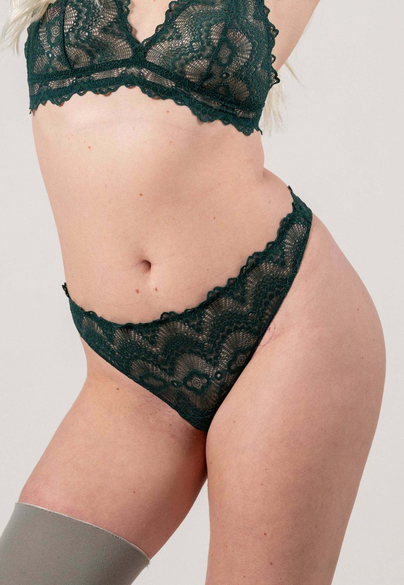 Lace bralette en string set in donkergroen. Met gegolfde randen en bloemenpatronen. Zachte textuur met transparante stof en verstelbare bandjes.