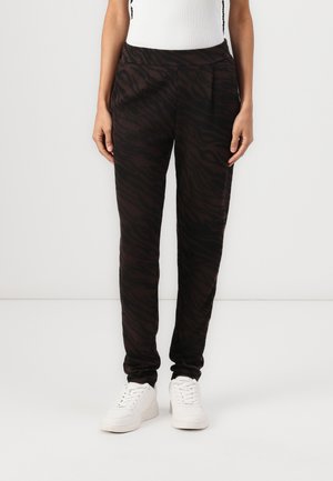 Svarte joggebukser med et brunt zebra-stripemønster, laget av myk stoff, med en smalere design og elastisk midje, sammen med hvite sko.