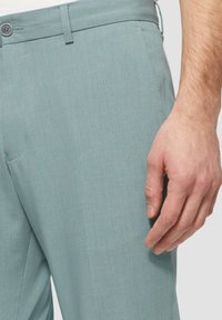 Helle blaue Stoffhose aus glattem Material, mit flachem Frontdesign, Seitentaschen und einer dezenten Textur. Bund mit Knopfverschluss.