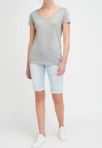 Szary, krótki t-shirt z dekoltem w serek, w połączeniu z jasnoniebieskimi, w paski, szortami do kolan. Model ma na sobie białe sneakersy i prostą naszyjnik.