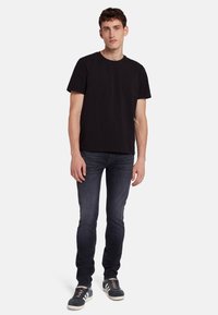 T-shirt nera in cotone con scollatura a girocollo, abbinata a jeans slim-fit blu scuro e sneakers grigie con accenti bianchi.