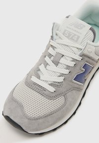 Grey athletic shoe with mesh and suede materials, featuring white laces, a purple logo, and a cushioned tongue for comfort.