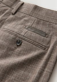 Braune strukturierte Stoffhose mit einer Gesäßtasche, die einen grauen Akzent und einen einzelnen Knopf aufweist. Der Stoff zeigt ein dezentes Muster.