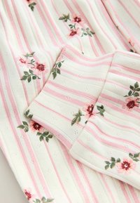 White fabric with pink stripes and small red and pink floral patterns, featuring a folded cuff detail.