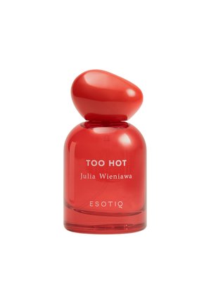Czerwona butelka perfum z etykietą "TOO HOT Julia Wieniawa ESOTIQ" z zaokrągloną, asymetryczną nakrętką na białym tle.