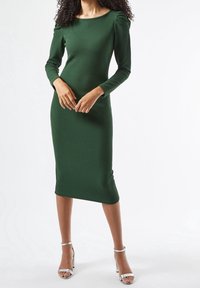 Vihreä ribattu pitkähihaine mekko, jossa on venepääntie ja kerrostettu olkatieto, polvipituinen, yhdistettynä hopeisiin nilkkaketjukenkiin.