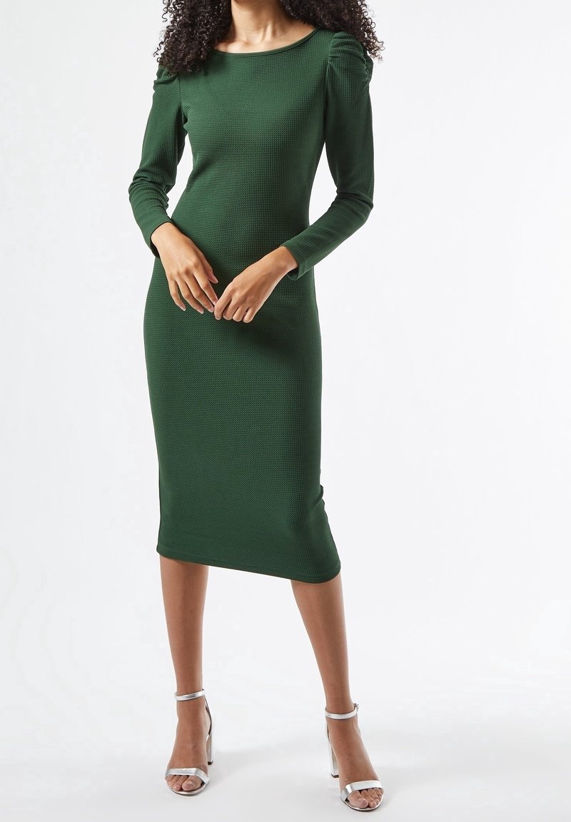 Vihreä ribattu pitkähihaine mekko, jossa on venepääntie ja kerrostettu olkatieto, polvipituinen, yhdistettynä hopeisiin nilkkaketjukenkiin.