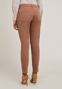 Pantaloni skinny-fit in un colore rosa smorzato, con vita alta, tasche posteriori e un tessuto liscio e elastico, abbinati a scarpe con tacco alto color sabbia.