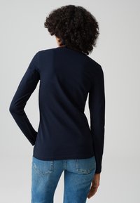 Maglietta a maniche lunghe blu navy con scollatura tonda, realizzata in tessuto morbido. Abbinata a jeans su misura azzurri. Texture liscia, design casual.