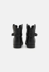 Botas de tobillo de cuero negro con punta redondeada, tirador trasero y detalle decorativo de correa. Textura lisa y tacones bajos en bloque.