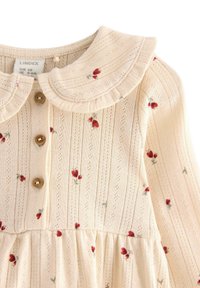 Beige blommönstrad klänning med volangkrage, knappfram och delikat stickad textur. Har små röda och gröna blommotiv.