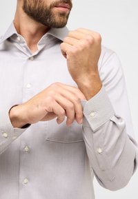 Lichtgrijs overhemd met knoopjes, voorzien van een textuurpatroon, een button-down kraag en linked cuffs; het heeft parelmoeren knopen en een borstzak.