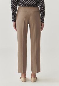 Beige tailored trousers with a high waist, straight legs, and back pockets, paired with a patterned long-sleeve shirt and beige shoes.