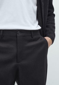 Zwarte geprinte broeken met een rechte voorkant en enkele knoopsluiting, gedragen met een effen witte t-shirt en een gestructureerde donkere cardigan.