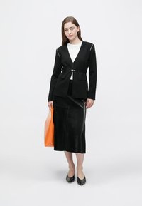 Čierne priliehavé sako na mieru so zipsovým detailom, doplnené čiernou koženou sukňou po kolená. Modelka nesie veľkú oranžovú kabelku a má na sebe čierne balerínky.