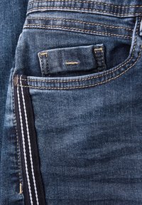 Jeans de denim en azul oscuro con una textura desgastada. Presentan un bolsillo trasero y doble costura en un color contrastante, con detalles de herrajes visibles.