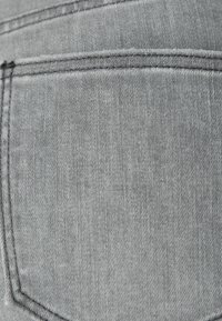 Tela de mezclilla gris con un bolsillo trasero y costura doble. La textura es suave, con un ligero brillo y un desgaste mínimo visible.