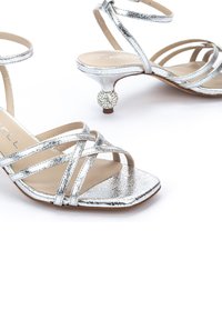 Sandalias plateadas con tiras, acabado metálico texturizado, punta cuadrada y un tacón decorativo de bola brillante. Plantilla interior de suave color beige.