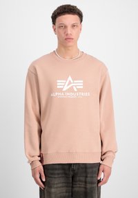 Sudadera rosa hecha de un tejido suave, con un logo y gráfico blancos en la parte delantera. Puños y dobladillo acanalados con una etiqueta en el lado inferior.