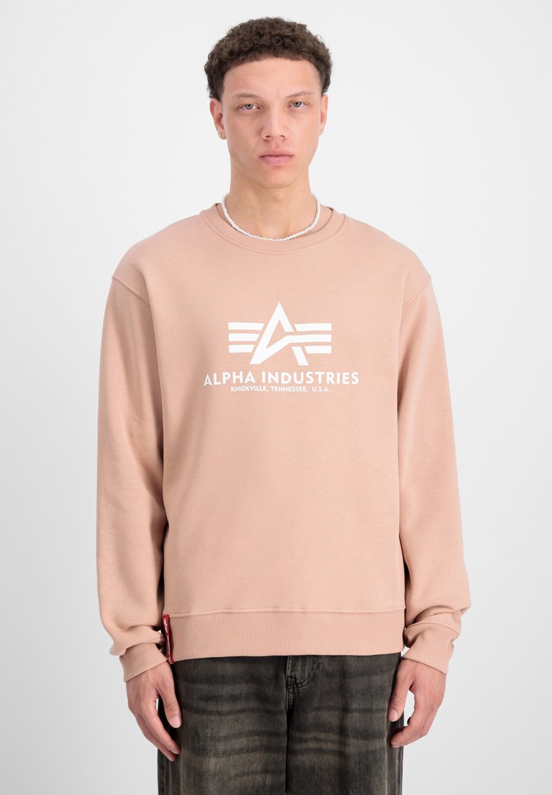 Sudadera rosa hecha de un tejido suave, con un logo y gráfico blancos en la parte delantera. Puños y dobladillo acanalados con una etiqueta en el lado inferior.