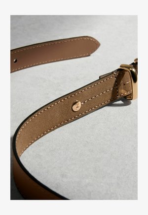 Barna bőröv részletes varrással, aranyszínű csattal és egy kis kör alakú fém emblémával, melyen gravírozott "Z" betű található, texturált felületen.