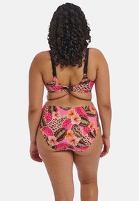 Bikini rose avec un imprimé floral et fruité, doté de bretelles noires. Bas taille haute et haut de soutien, mettant en avant des couleurs et motifs éclatants.