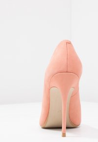 Chaussure à talons hauts en daim rose avec un bout pointu, une silhouette épurée et un talon aiguille fin. La semelle est beige avec un détail de logo subtil.
