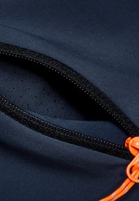 Taschina in tessuto navy con zip nera e tiraz zipper arancione vivace, presenta un rivestimento testurizzato con piccole perforazioni per la traspirabilità.