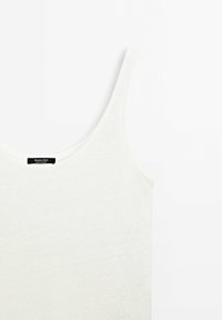 White cotton tank top with wide straps, featuring a smooth texture and a rounded neckline. Brand label visible near neck.