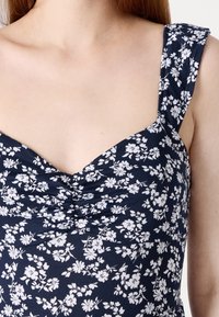 Navy floral dress with white floral patterns, featuring a sweetheart neckline and wide straps, gathered texture at the bust.