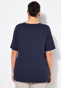 Marinblå kortärmad topp med rund halsringning och avslappnad passform. Mjuk material, fållen slutar vid höfterna, med dekorativ utskärning på axlarna.