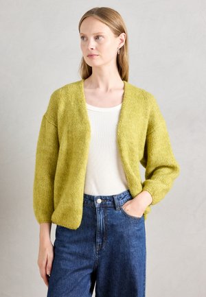 Grønn, strikket cardigan med løs passform, senkede skuldre og teksturert stoff. Brukt over en lys topp og smale blåjeans.