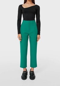 Maglietta nera a maniche lunghe e pantaloni verdi a vita alta con taglio dritto. I pantaloni presentano pieghe frontali. Mocassini neri con zeppa completano il look.